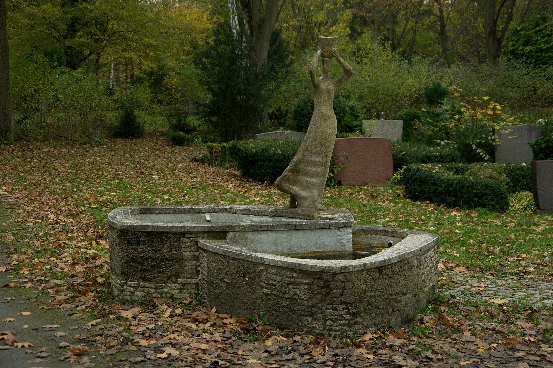 Skulpturaler Brunnen zwischen Bäumen auf dem Parkfriedhof Neukölln